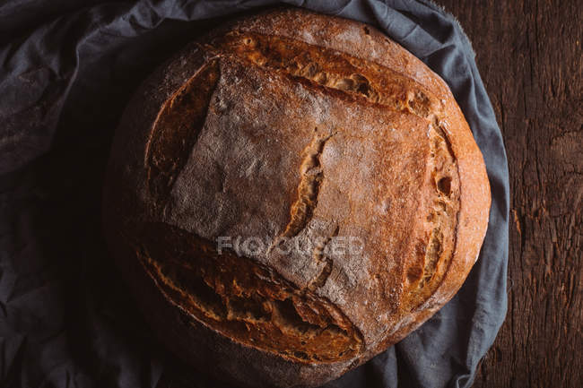 Rustic loaf of artisan bread on dark canvas — Stock Photo