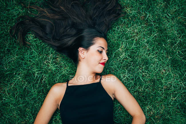 Cheerful brunette woman lying in grass and looking aside — Stock Photo