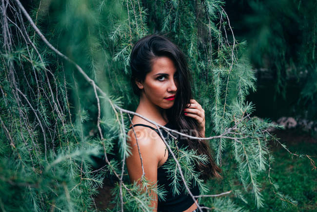 Brunette woman in fir branches looking at camera — Stock Photo