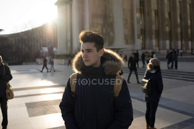Pensive young tourist standing on big square in sun flare and looking away. — Stock Photo