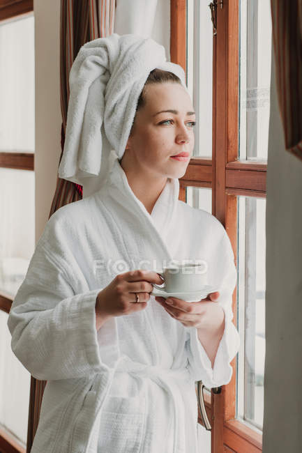 Thoughtful woman having coffee after bath and looking at camera — Stock Photo