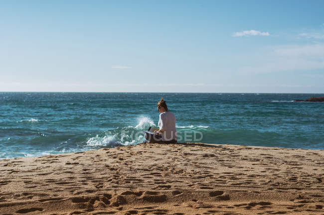 Зрелая женщина сидит на берегу моря и читает книгу в солнечный день — стоковое фото