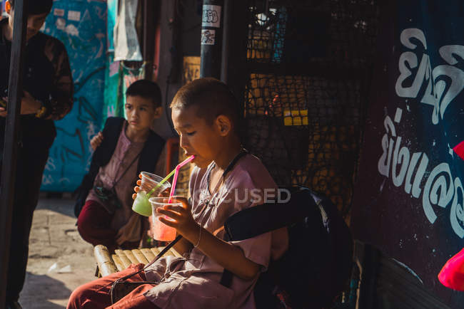 CHIANG RAI, THAILAND- FEVEREIRO 9, 2018: Vista lateral da adolescente sentada na rua e bebendo coquetéis refrescantes . — Fotografia de Stock