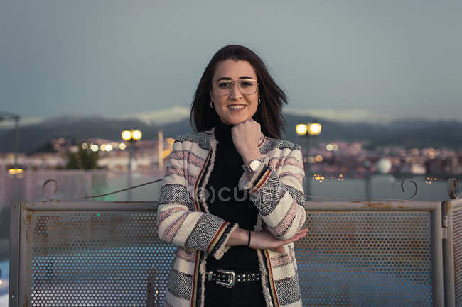 Cheerful pretty woman in glasses leaning on concrete fence and looking at camera — Stock Photo