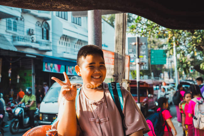 CHIANG RAI, TAILANDIA - 9 DE FEBRERO DE 2018: Niño regordete alegre haciendo un gesto de dos dedos en la calle de la ciudad . - foto de stock