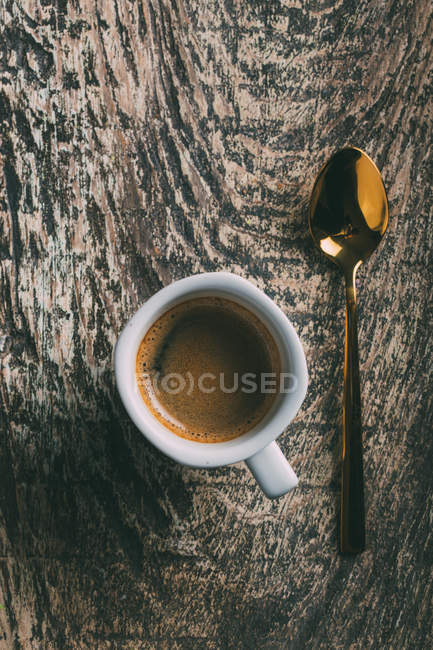 Прямо над видом на чашку кофе и ложку на деревенском деревянном столе — стоковое фото
