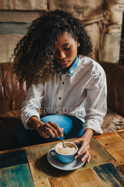 Mujer bastante joven revolviendo taza de café en la mesa . - foto de stock