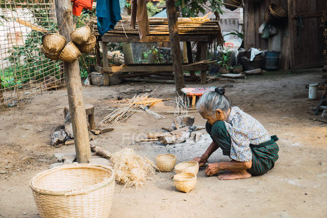 LAOS- 18 DE FEBRERO DE 2018: Vista lateral de la mujer mayor sentada y haciendo cestas . - foto de stock