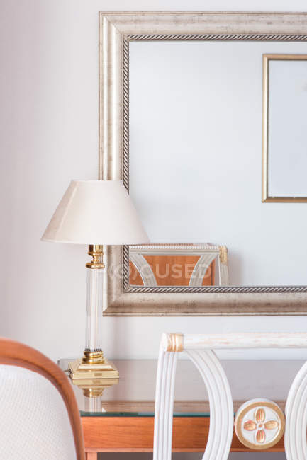 Mesa com lâmpada e espelho refletindo cadeira — Fotografia de Stock