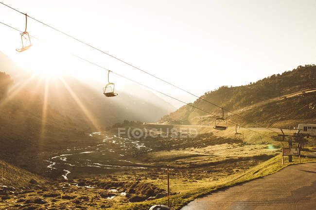 Picturesque view to empty ropeway moving over green mountains in sunset lights. — Stock Photo