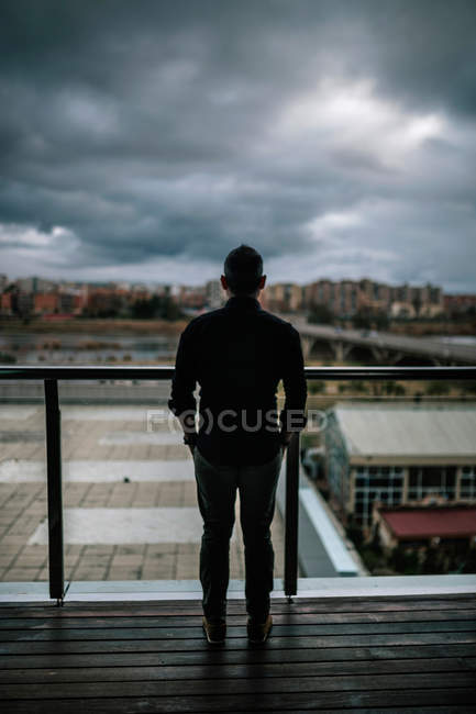 Silhouette of man standing at handrail over cloudy cityscape ...