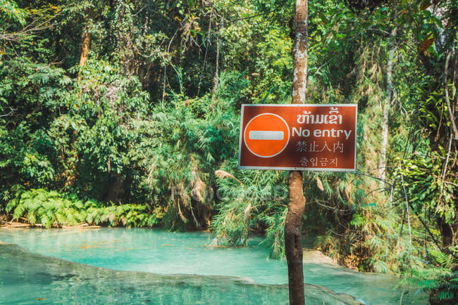Нет входа запретный знак висит на столбе на голубом озере в джунглях — стоковое фото