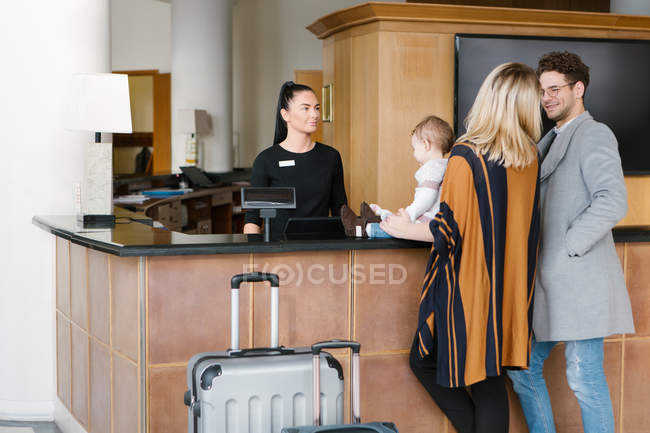 Family with child and suitcases talking with staff at reception in hotel. — Stock Photo