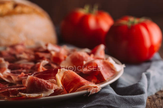 Still life of ham with tomatoes by bread on table — Stock Photo