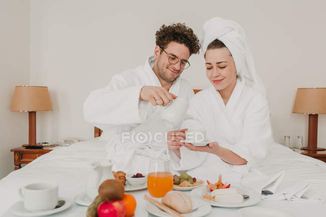 Веселая пара завтракает в гостиничной постели — стоковое фото