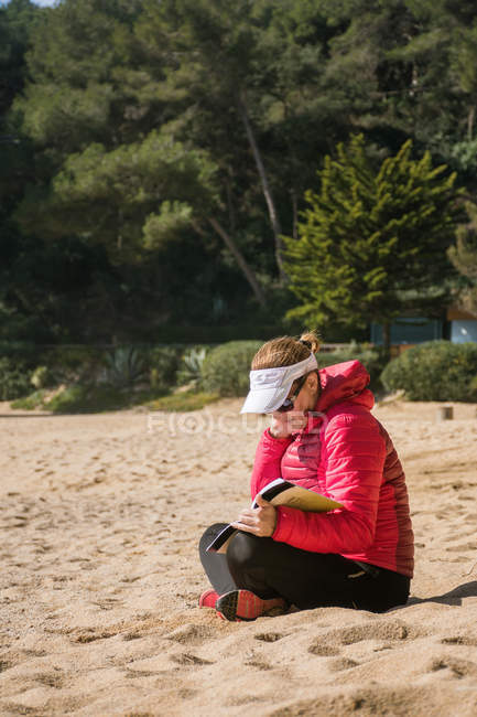 Вид сбоку читающей женщины на песчаном пляже — стоковое фото