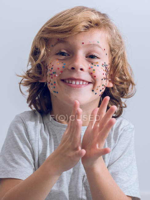 Chico alegre con confeti en la cara aplaudiendo las manos - foto de stock