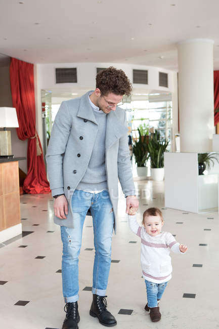 Homem bonito feliz andando com a criança pequena no salão grande . — Fotografia de Stock
