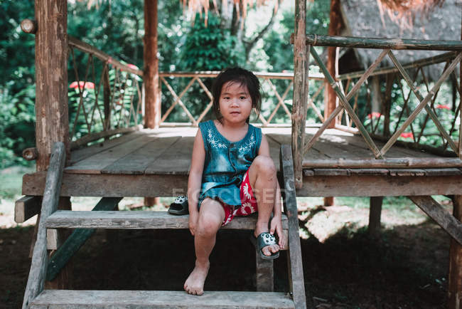 LAOS, LUANG PRABANG: Niño sentado en la cabaña y mirando a la cámara - foto de stock