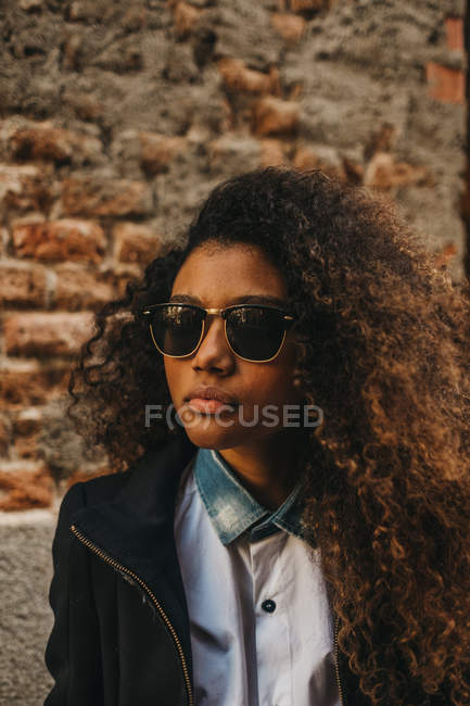 Femme élégante en lunettes de soleil posant au mur de briques — Photo de stock