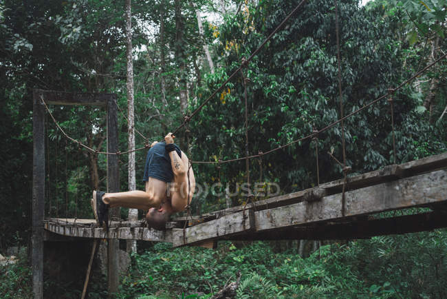 Man hanging upside down on rope of bridge — Stock Photo