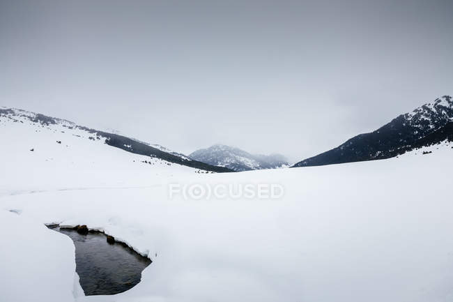 Snowy landscape of mountain valley over misty peak and grey sky — Stock Photo