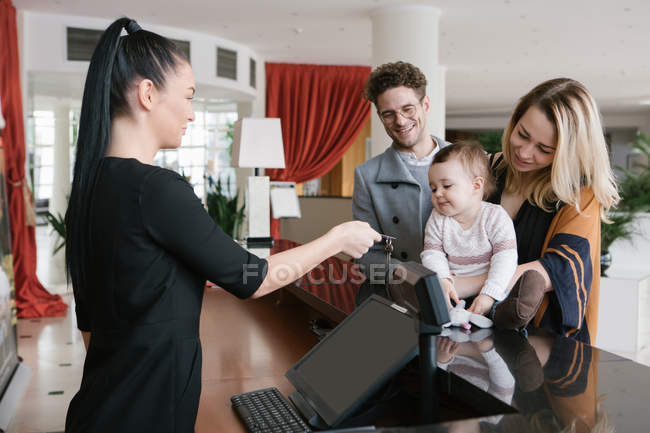 Side view of hotel staff worker giving room key to happy family. — Stock Photo