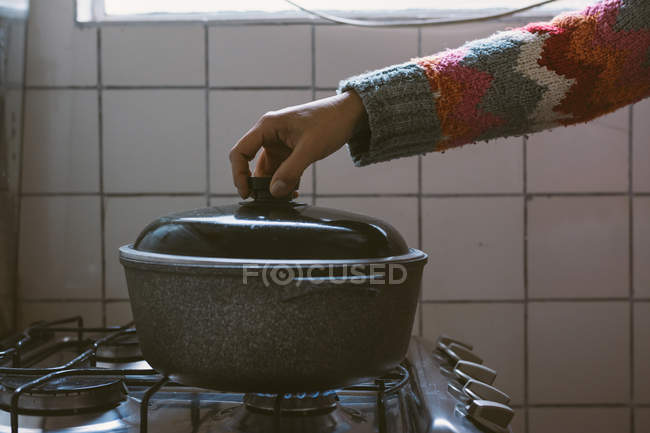 Crop female hand holding lid of pot on stove — Stock Photo