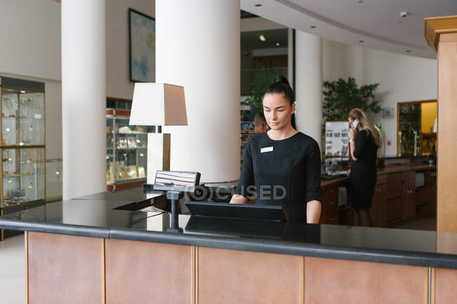 Гарненька брюнетка готель працівник стоїть на рецепції — стокове фото
