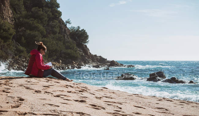 Mulher madura lendo livro na praia ensolarada — Fotografia de Stock