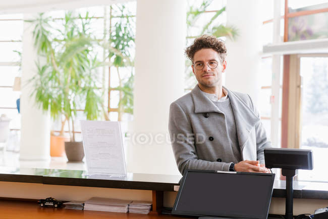 Hombre sonriente en gafas de pie en la recepción - foto de stock