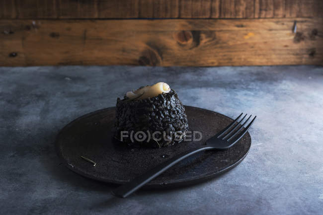 Schwarzer Reis mit Tintenfisch auf schwarzem Teller — Stockfoto