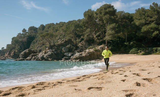 Мужчина бегает по морю на песчаном пляже в солнечный день — стоковое фото