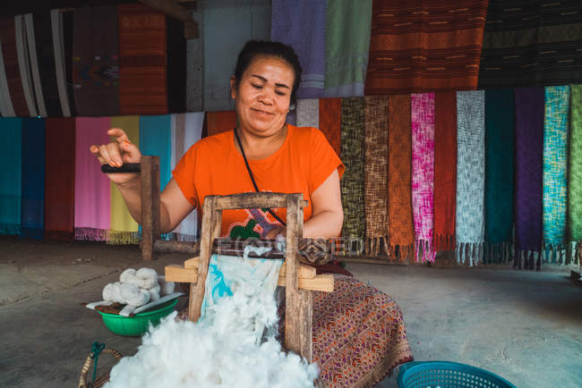 LAOS- 18 FÉVRIER 2018 : Femme asiatique joyeuse assise dans un magasin et travaillant avec du tissu . — Photo de stock