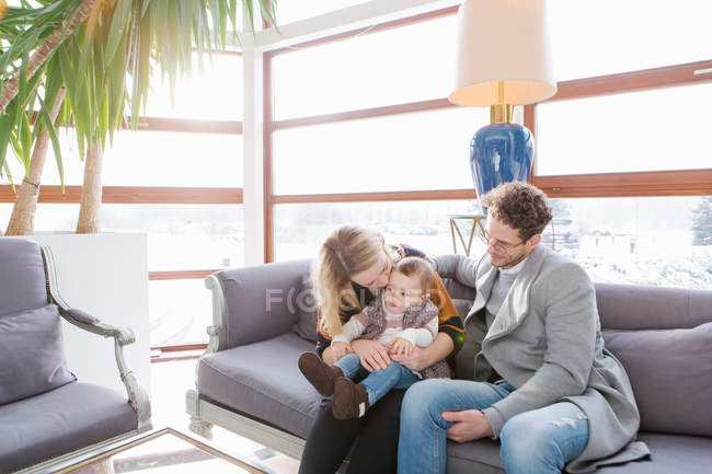 Cheerful family sitting on couch and kissing child — Stock Photo