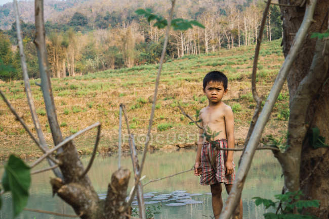 LAOS- FEBRERO 18, 2018: Niño pensativo de pie en la naturaleza y mirando a la cámara . - foto de stock