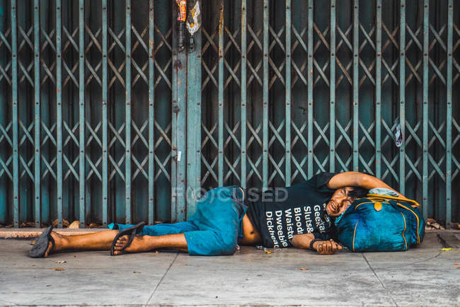CHIANG RAI, TAILANDIA - 12 DE FEBRERO DE 2018: Hombre sin hogar acostado en una bolsa como almohada en la acera - foto de stock