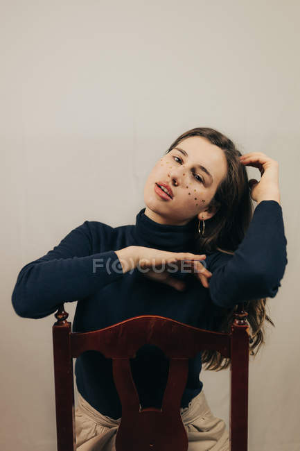 Brunette woman with glitters on face sitting on chair and looking at camera — Stock Photo