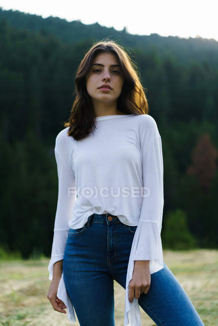 Junge Frau blickt in die Kamera, während sie auf einer Wiese in der Natur steht. — Stockfoto