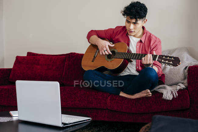 Jovem tocando guitarra na frente do laptop em casa — Fotografia de Stock