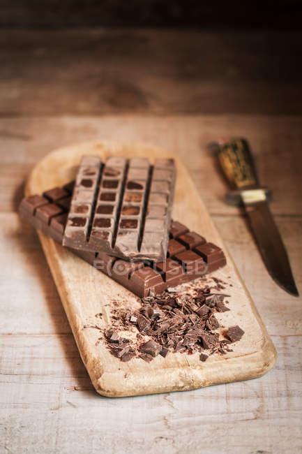 Barre e scaglie di cioccolato sul tagliere di legno — Foto stock