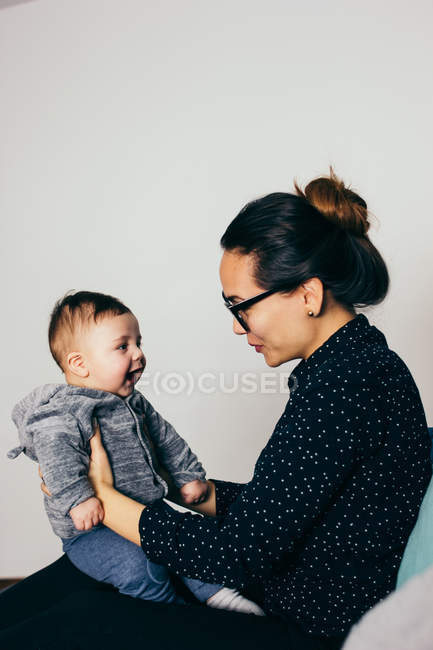 Vista lateral del adorable niño en las manos de la madre en el entrenador en casa - foto de stock