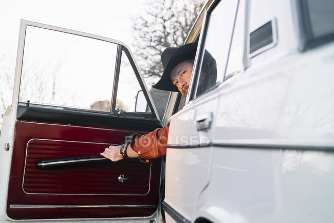 Продуманий чоловік у капелюсі сидить у білому старовинному автомобілі зачинені двері — стокове фото
