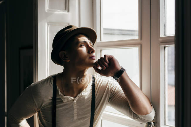 Hombre de ensueño con sombrero mirando a la ventana . - foto de stock