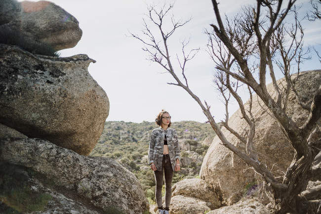 Молода жінка стоїть серед скель і голе дерево на природі — стокове фото