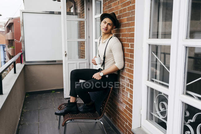 Man in hat drinking coffee on chair at balcony — Stock Photo