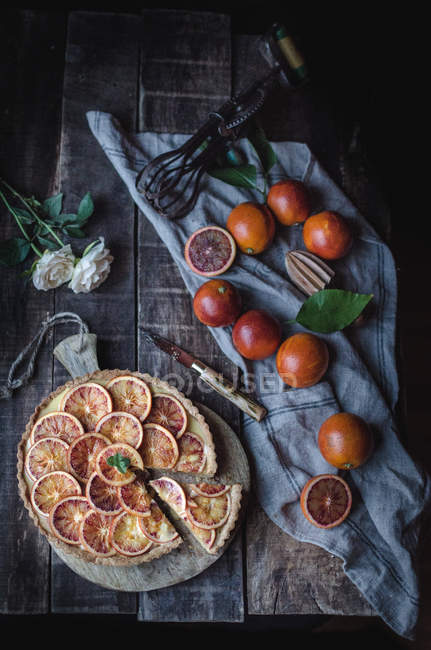 Сверху аппетитный пирог подается с красными апельсинами на деревенском столе . — стоковое фото