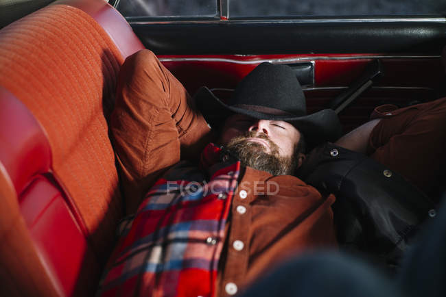 Homem de chapéu e camisa quadriculada dormindo em carro vintage — Fotografia de Stock