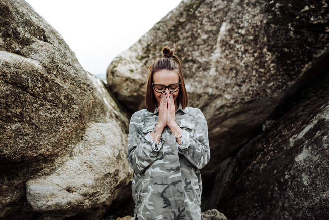 Молодая женщина в очках стоит у камней и молится с закрытыми глазами . — стоковое фото