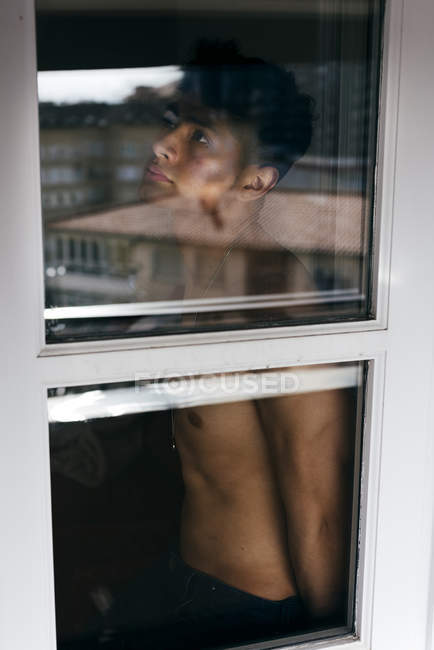Uomo senza maglietta posa dietro la finestra — Foto stock